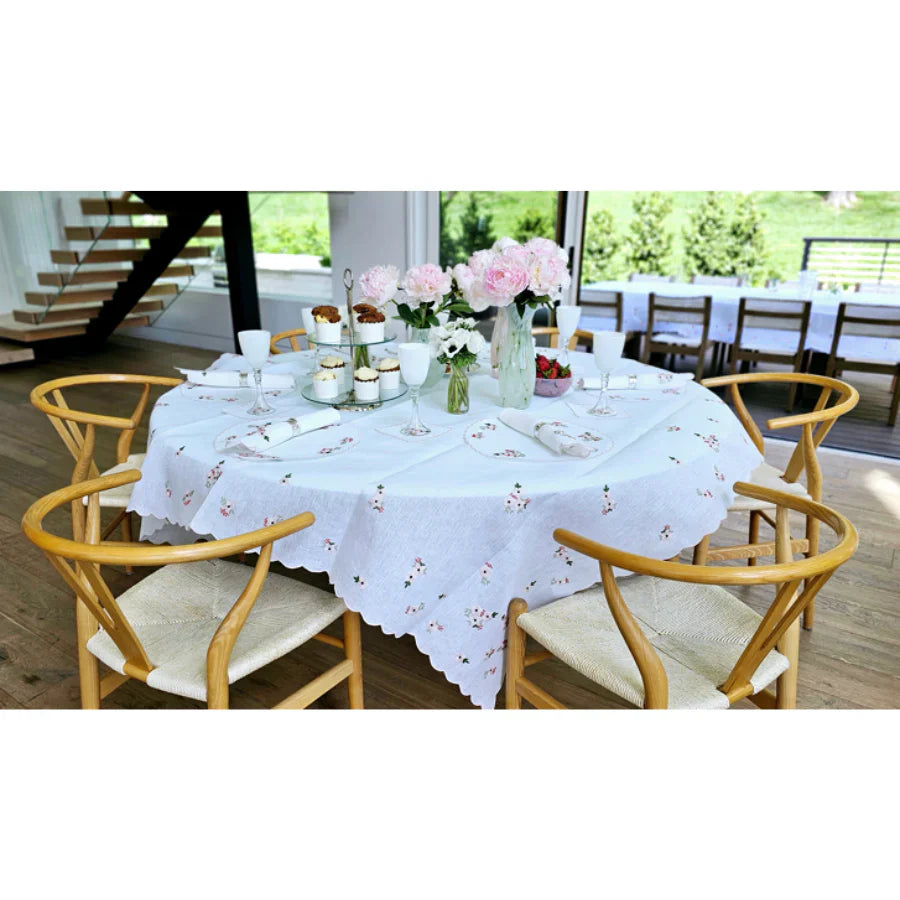 Elegant dining table with floral embroidered tablecloth, wooden chairs, and fresh flowers, ideal for home décor and gift inspiration from DecoDine.