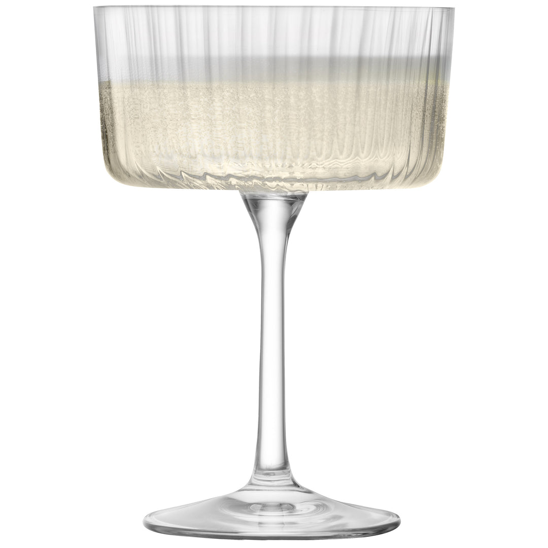 Elegant clear champagne cocktail glass with subtle textured lines, filled, on white background